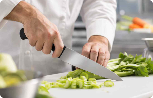 Chef chopping celery on a white board with a Victorinox stainless steel chef’s knife in a commercial kitchen